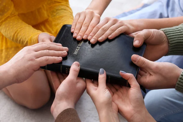 Group of people praying with Holy Bible on floor, closeup