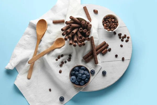 Composition with delicious chocolate wafer rolls, blueberries and coffee beans on blue background