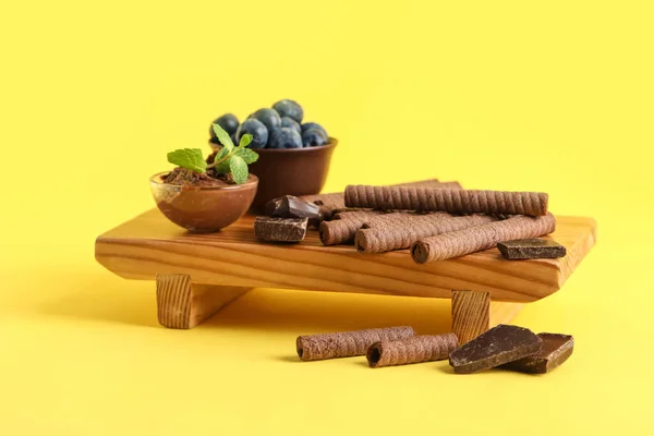 Board Delicious Wafer Rolls Chocolate Pieces Blueberries Yellow Background — Stockfoto