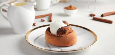 Plate with tasty cinnamon roll on light table