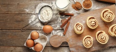 Pişmemiş tarçınlı rulo ve ahşap arka planda malzemeler.