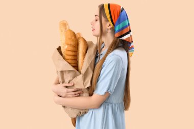 Young woman with fresh baguettes on beige background