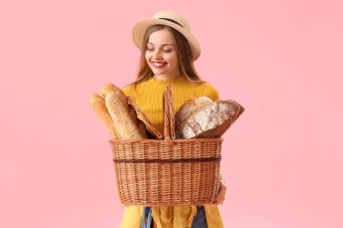 Young woman in hat with basket of fresh bread on pink background