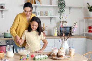 Little girl and her mother making dough for Easter cake in kitchen