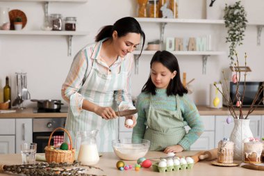 Little girl and her mother making dough for Easter cake in kitchen