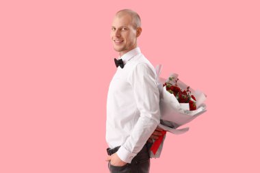Young man with bouquet of flowers on pink background. Valentine's Day celebration