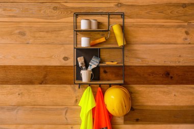 Shelf with builder's supplies and reflective vests on wooden wall