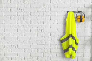 Reflective vest and hearing protectors on white brick wall