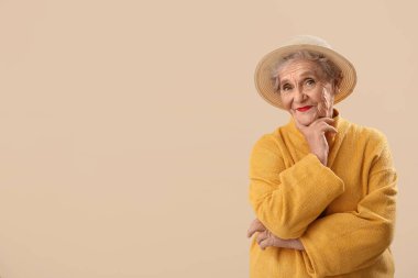 Thinking senior woman in hat on beige background