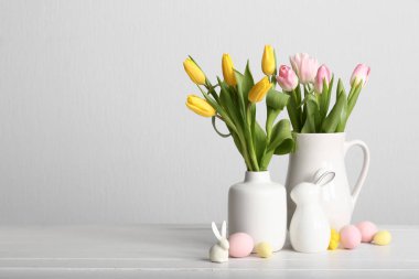 Vases with beautiful tulip flowers, ceramic bunnies and Easter eggs on light wooden table