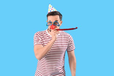 Handsome man in funny disguise with party blower on blue background. April Fools' Day celebration