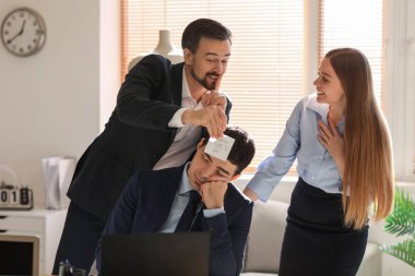 Young man and woman playing a prank on their sleeping colleague in office. April Fools' Day celebration