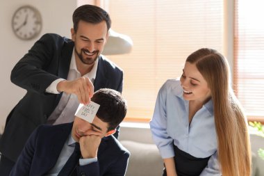 Young man and woman playing a prank on their sleeping colleague in office. April Fools' Day celebration