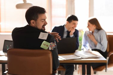 Sticky notes on back of young man sitting in office. April Fools' Day celebration