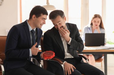 Young men with whoopee cushion laughing in office. April Fools' Day celebration