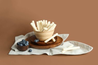 Bowls with delicious wafer rolls and blueberries on brown background