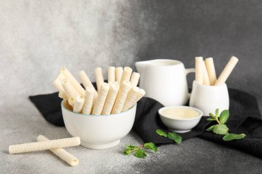 Bowls with delicious wafer rolls and condensed milk on grunge dark background
