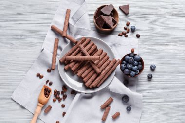 Plate with delicious chocolate wafer rolls and blueberries on grey wooden background