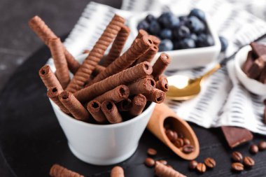 Bowl with delicious wafer rolls on black wooden board