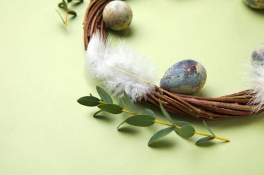 Composition with Easter eggs, wreath, eucalyptus branches and feathers on green background, closeup
