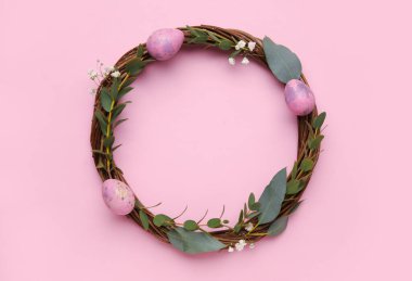 Easter wreath decorated with eggs and eucalyptus branches on color background