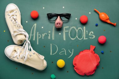 Composition with text APRIL FOOL'S DAY, shoes and party decor on blackboard
