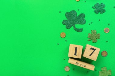 Calendar with date of St. Patrick's Day, coins and clovers on green background