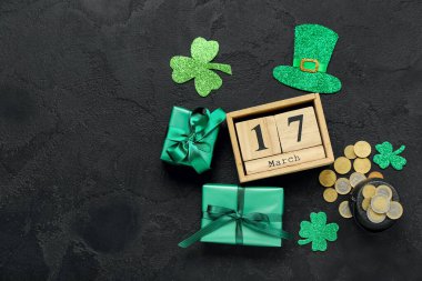 Calendar with date of St. Patrick's Day, gifts, coins and decor on dark background