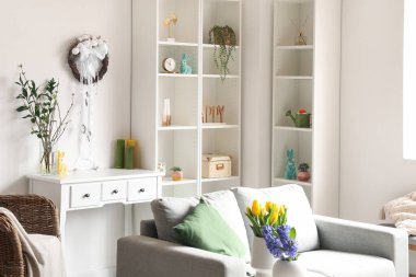 Interior of light living room with Easter wreath, sofa and shelving unit