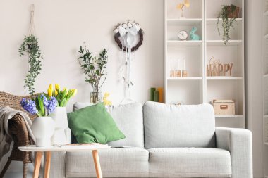 Interior of light living room with Easter wreath, sofa and shelving unit