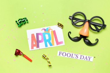 Composition with text APRIL FOOL'S DAY, party decor and serpentine on green background