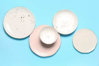 Set of empty ceramic plates on color background