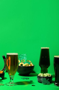 Glasses of beer, snacks and decor on green background. St. Patrick's Day celebration