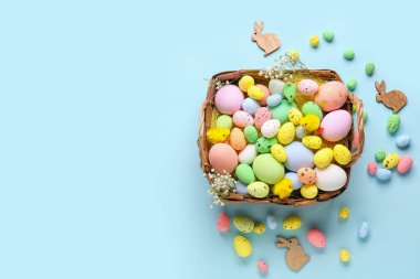 Composition with basket of different Easter eggs, toy chicks and gypsophila flowers on color background