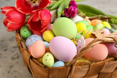 Basket with painted Easter eggs, decor and tulip flowers on grunge background, closeup