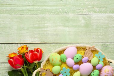 Basket with painted Easter eggs, decor and flowers on color wooden background