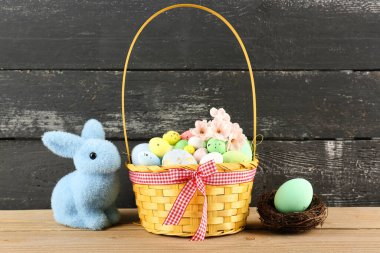 Basket with painted Easter eggs, flowers and toy bunny on wooden table
