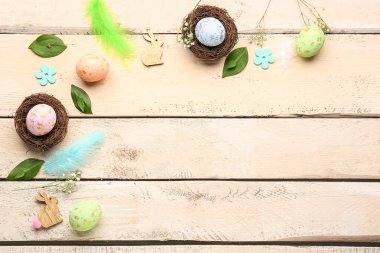 Composition with Easter eggs, feathers, plant leaves and gypsophila flowers on light wooden background