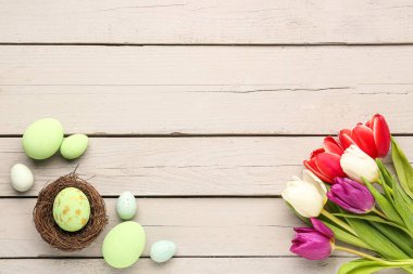 Composition with bouquet of beautiful tulip flowers and Easter eggs on light wooden background
