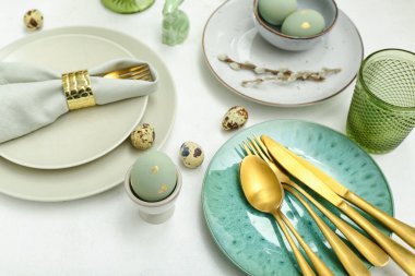 Stylish table setting, with Easter eggs, willow branches and golden cutlery on light background, closeup