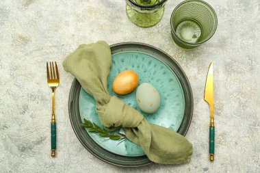 Table setting with Easter eggs, green leaves and cutlery on grey grunge background