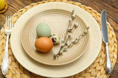 Table setting with Easter eggs and pussy willow branches on wicker mat, closeup