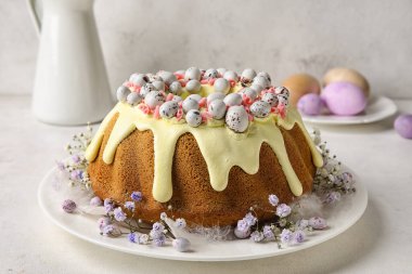 Plate with tasty Easter cake and gypsophila flowers on light background