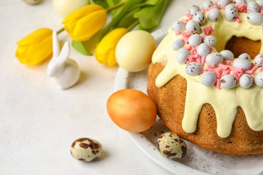 Plate with tasty Easter cake, eggs and tulip flowers on light background, closeup