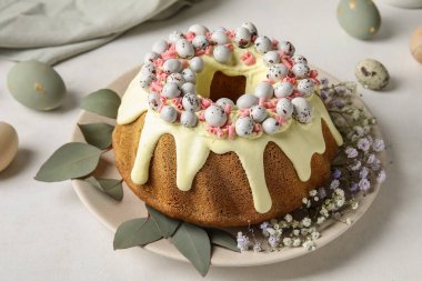 Plate with tasty Easter cake, eggs and gypsophila flowers on light table