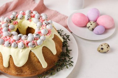 Plate with tasty Easter cake, eucalyptus branches and eggs on light table, closeup