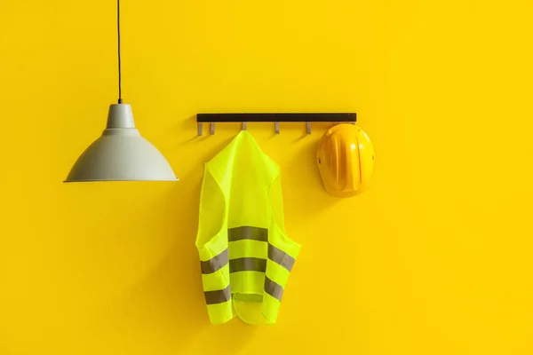 Reflective vest and hardhat hanging on yellow wall
