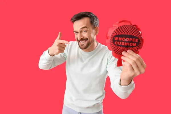 Handsome Man Pointing Whoopee Cushion Red Background April Fools Day — Zdjęcie stockowe