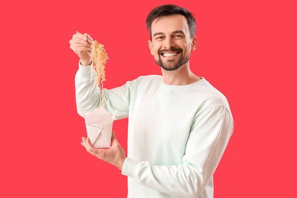 Handsome man with box of Chinese noodles on red background