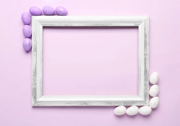 Composition with empty picture frame and Easter eggs on lilac background